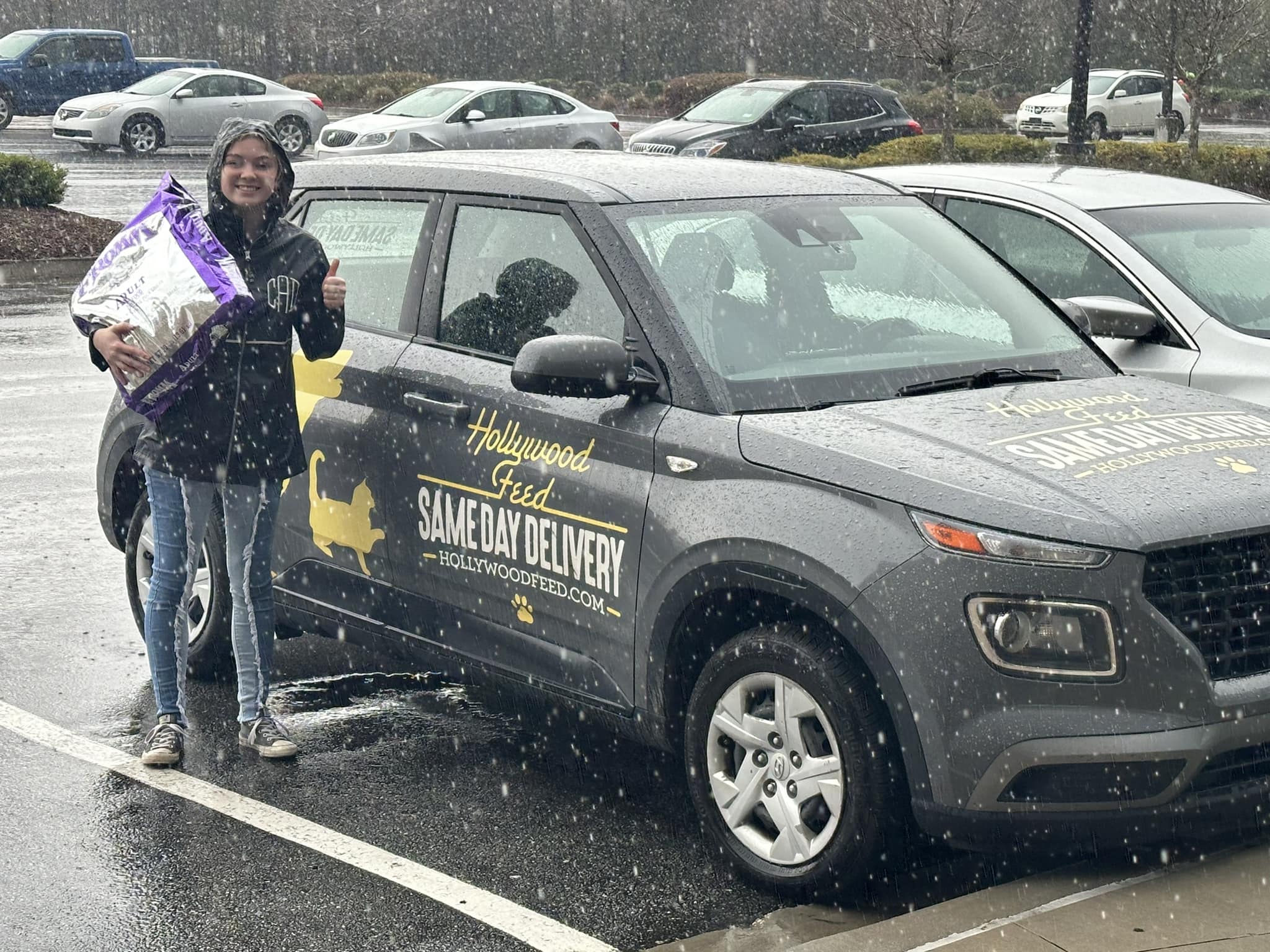 Girl carrying Fromm dog food in the rain next to a gray Same Day Delivery car
